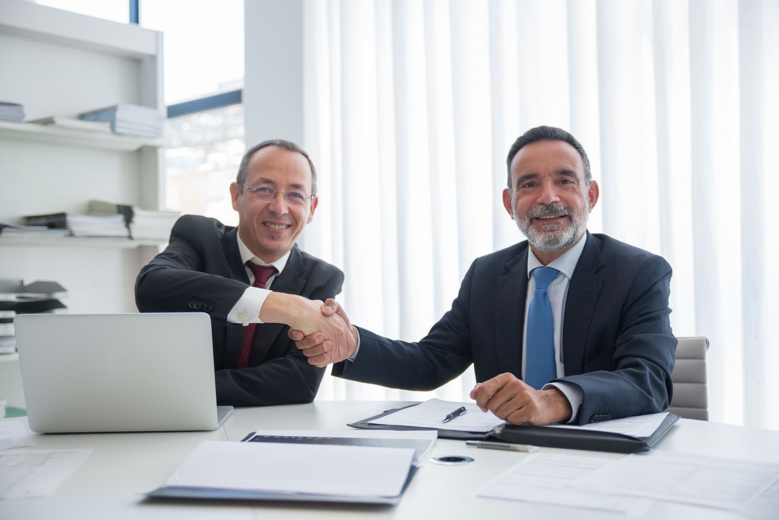 Two business owners shaking hands across a desk after agreeing to work together