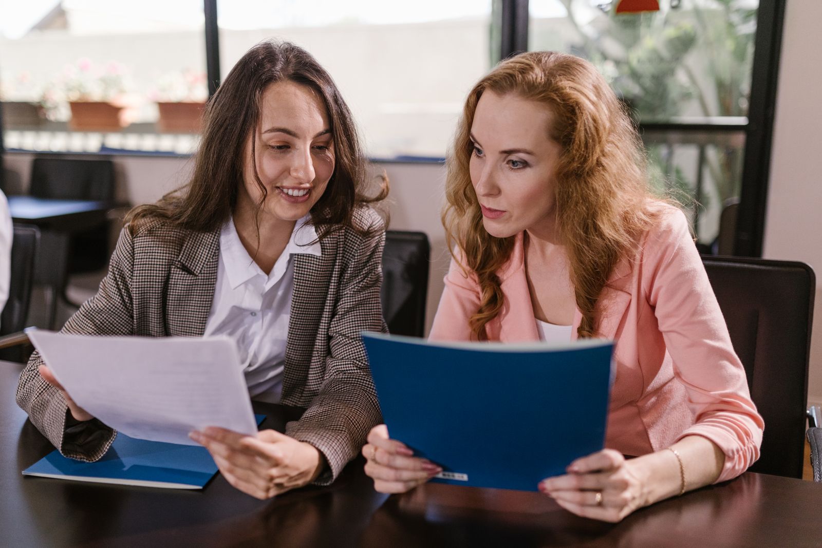 Two colleagues comparing a printed page and a blue folder side by side at a table
