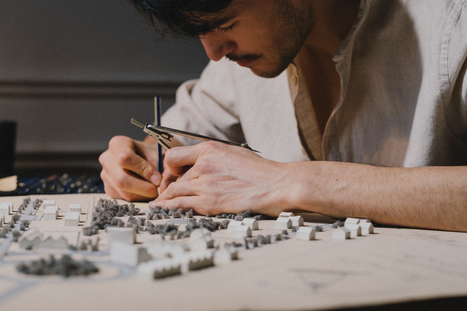 An architect working with a compass over a white site model of houses and trees