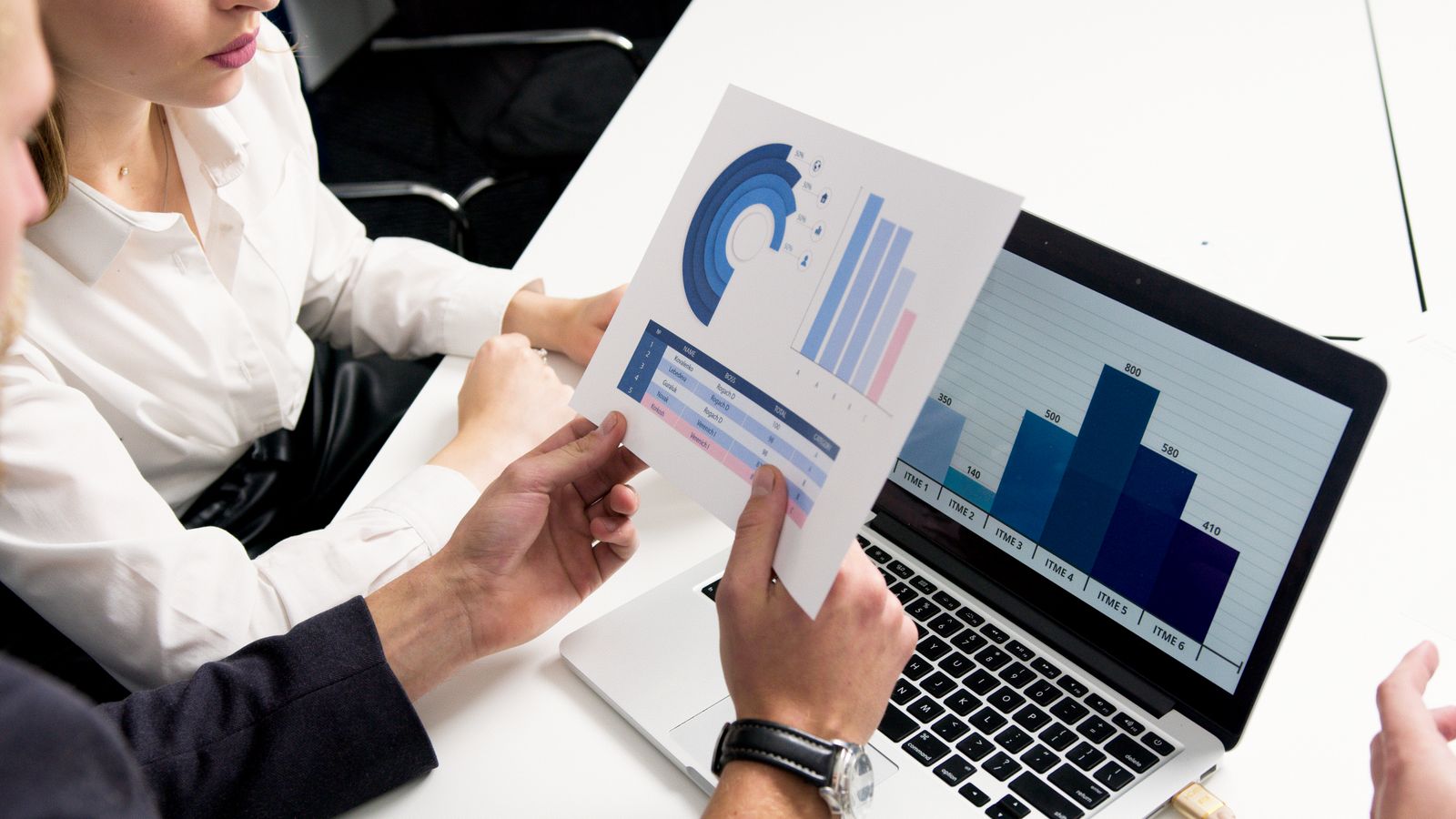 Two colleagues reviewing printed charts and a laptop showing a bar graph