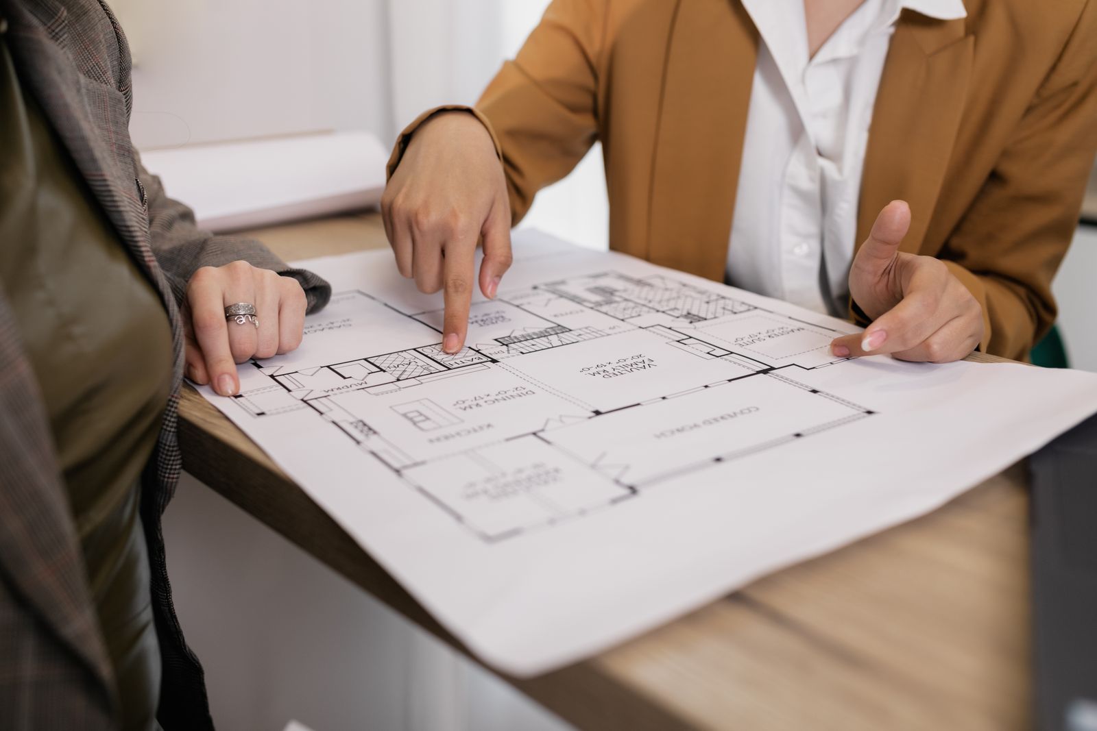 Two people reviewing a printed custom home floor plan with a master suite, vaulted family room, and covered porch
