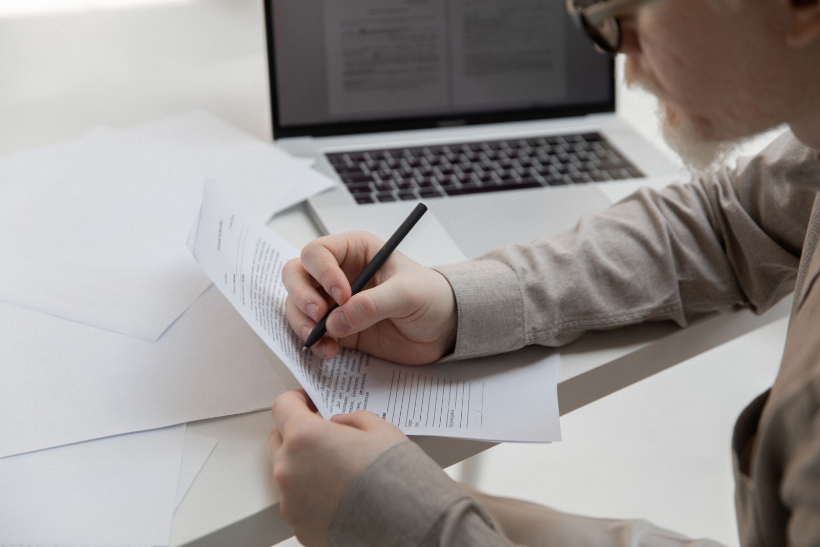 Person marking up a printed draft with a pen next to an open laptop