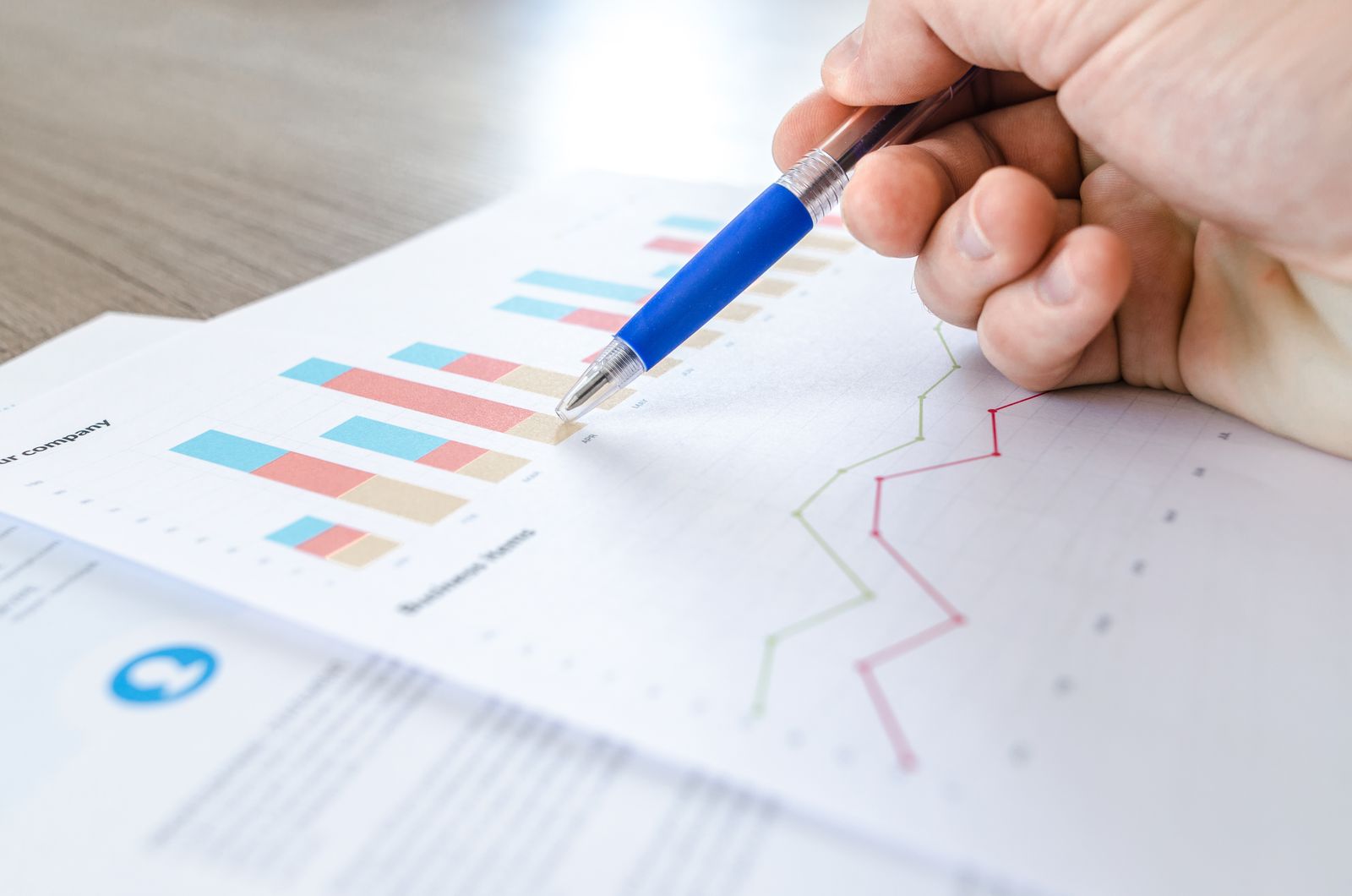 A hand annotating printed charts and graphs during a cost analysis