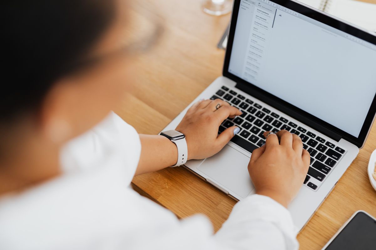 Life coach typing a weekly email newsletter to her subscriber list on a laptop