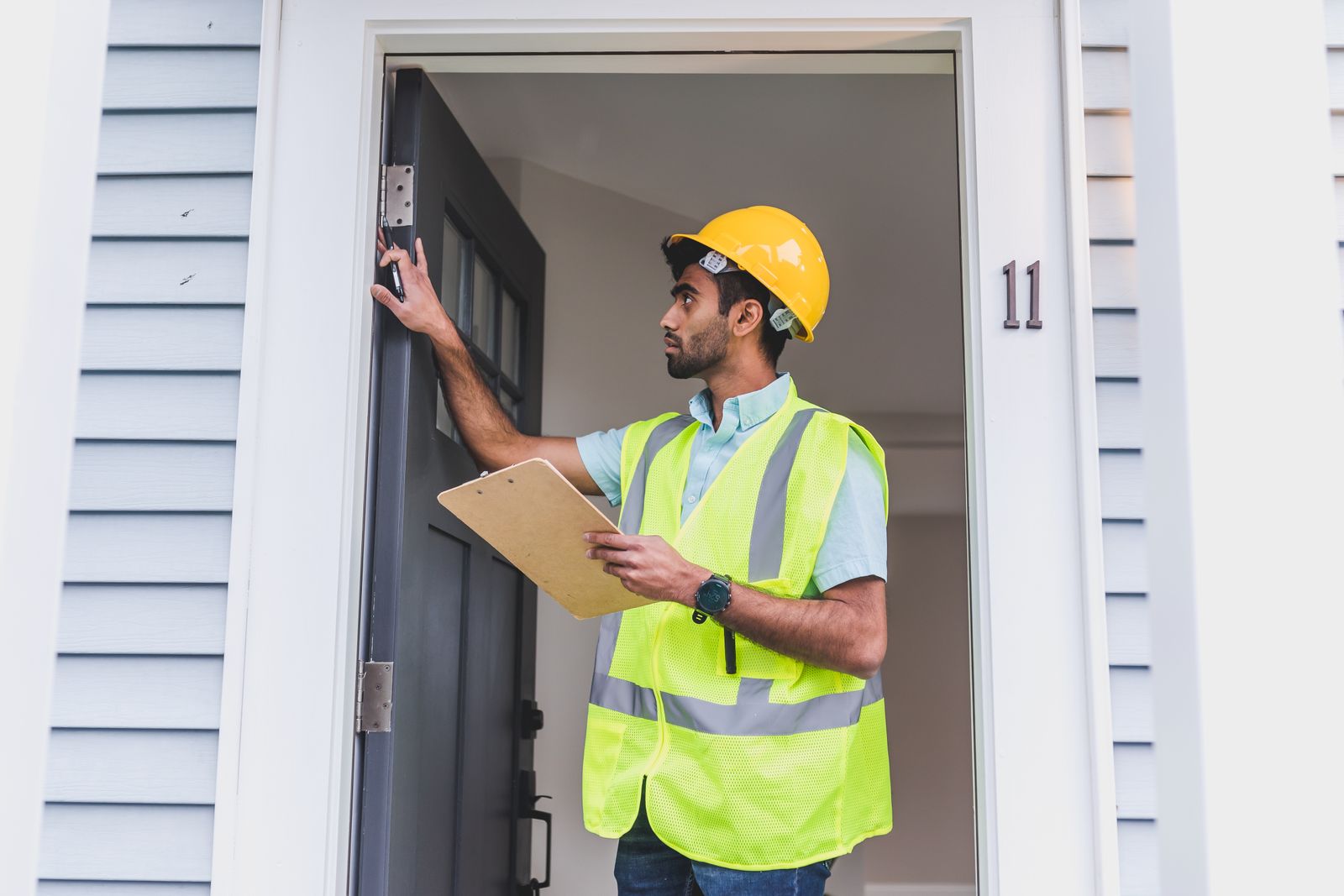 A screened service professional with a clipboard inspecting the front door of a home