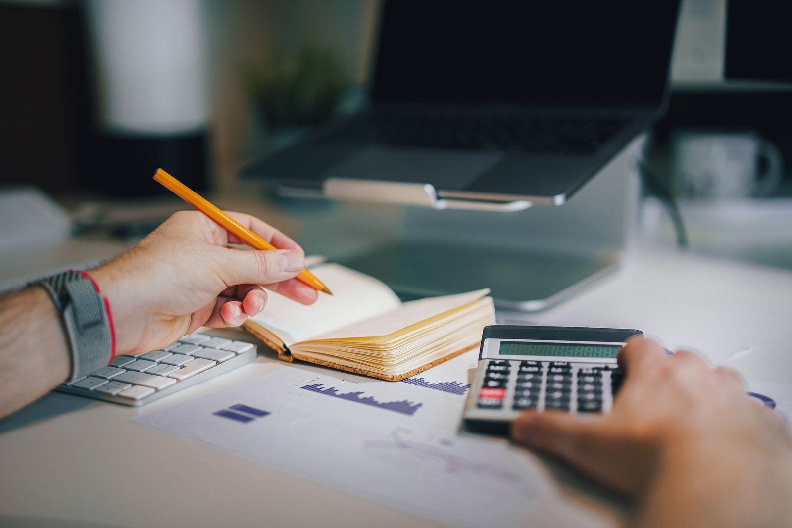 Hands working through figures with a calculator, notebook and charts on a desk