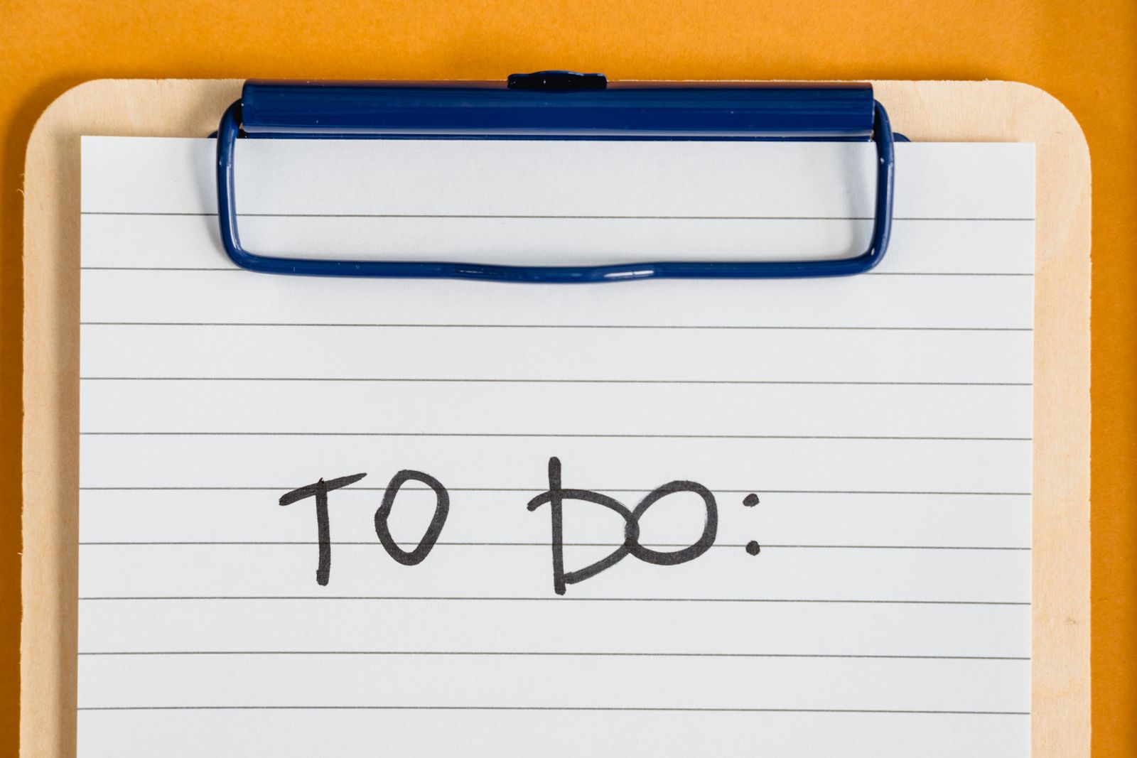 A clipboard with a handwritten to do list on an orange background