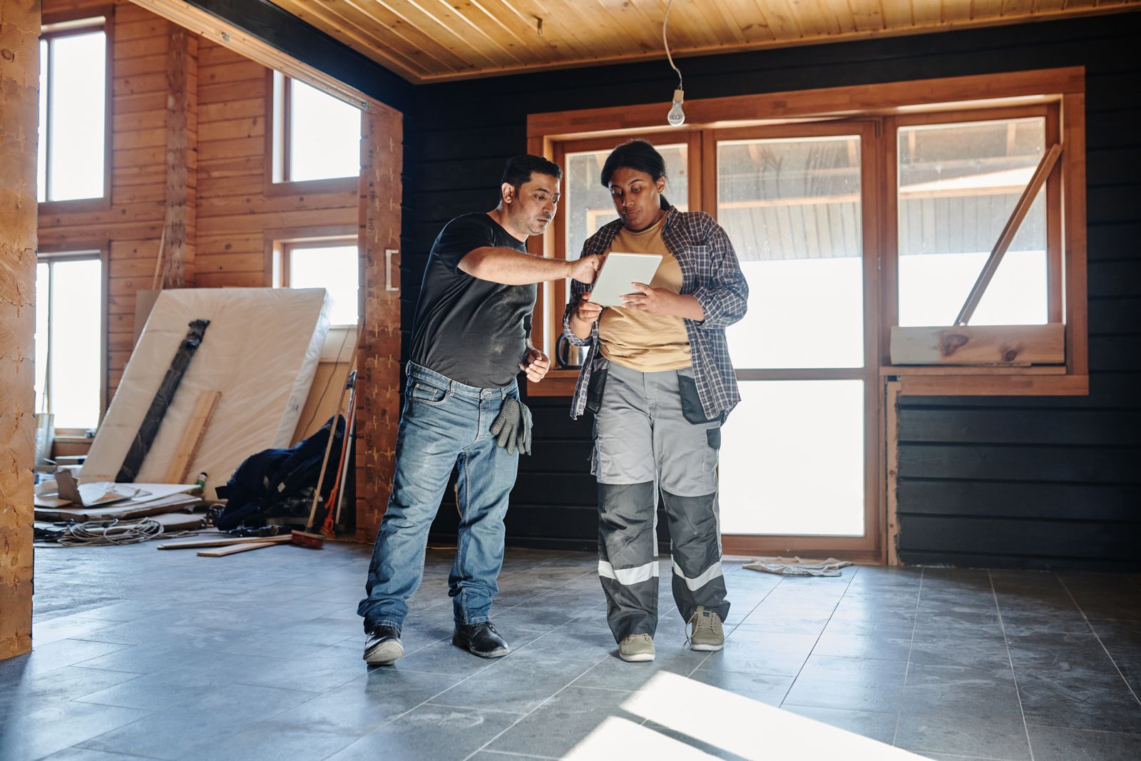 Two contractors reviewing plans on a tablet inside a house under renovation