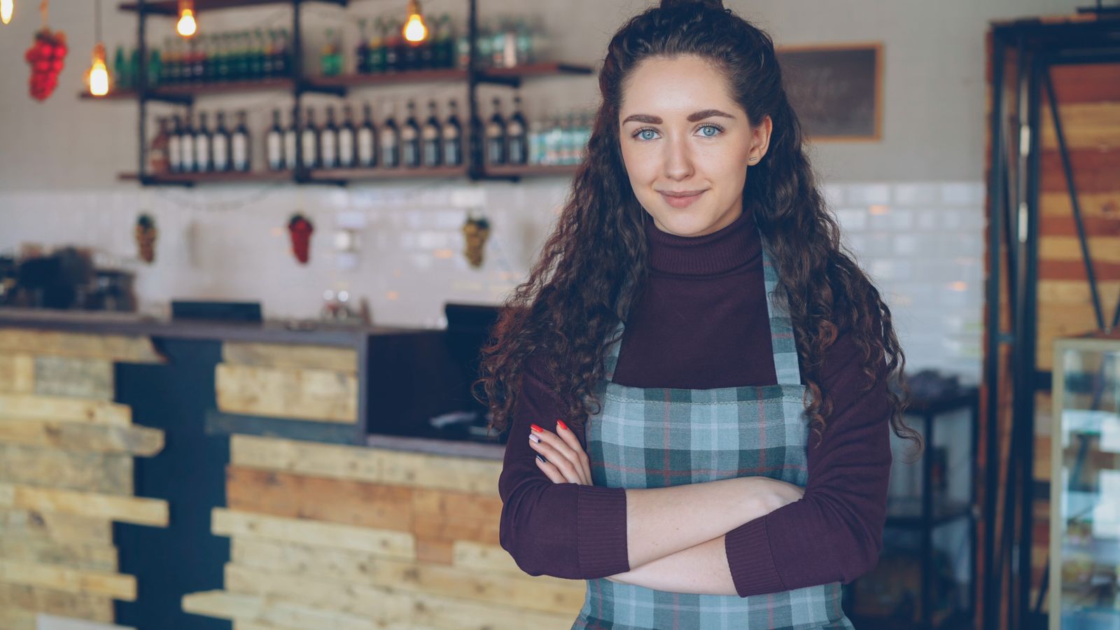 Small cafe owner in an apron standing with arms crossed in front of the shop counter