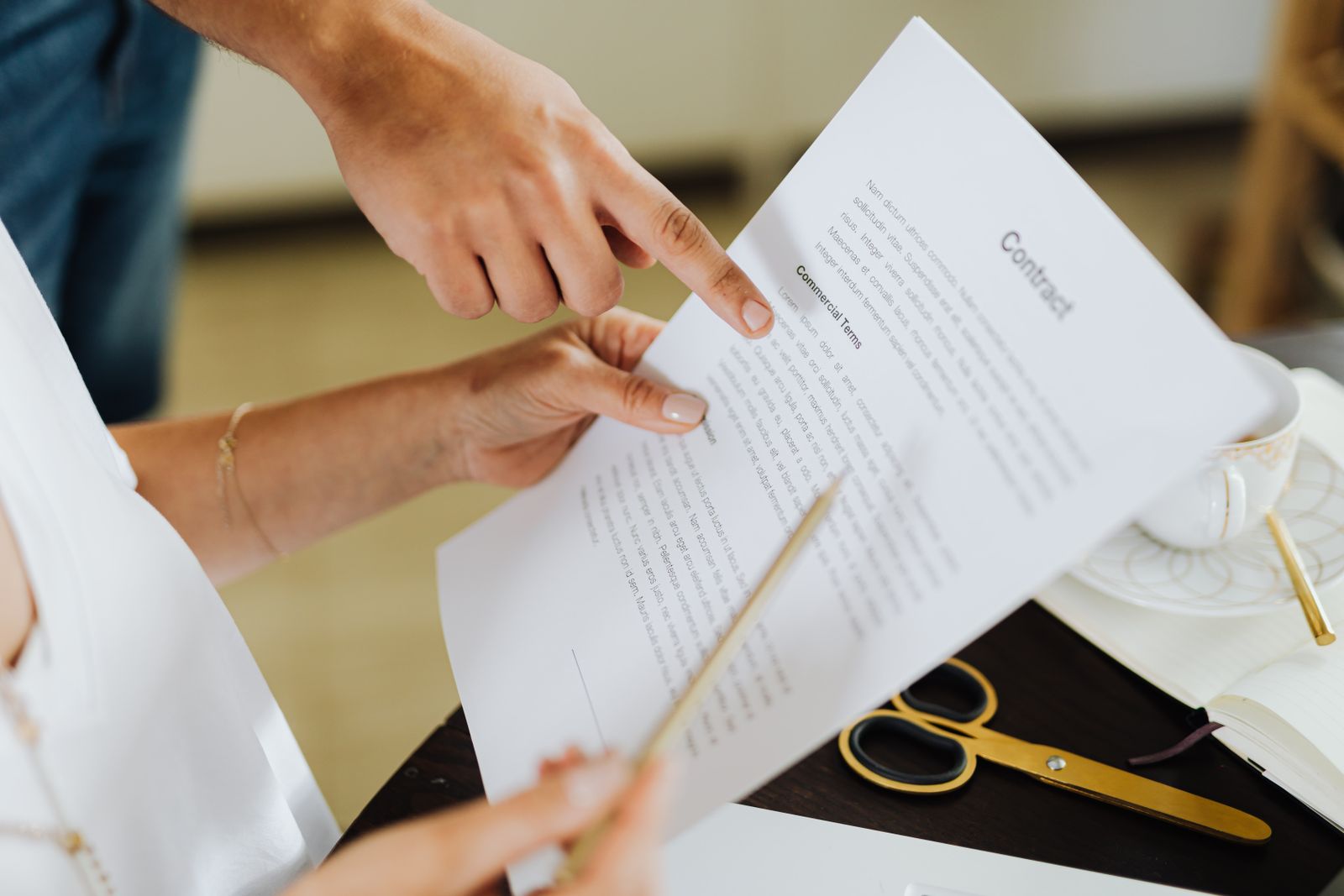 Two people reviewing the commercial terms of a printed contract, one pointing at a clause