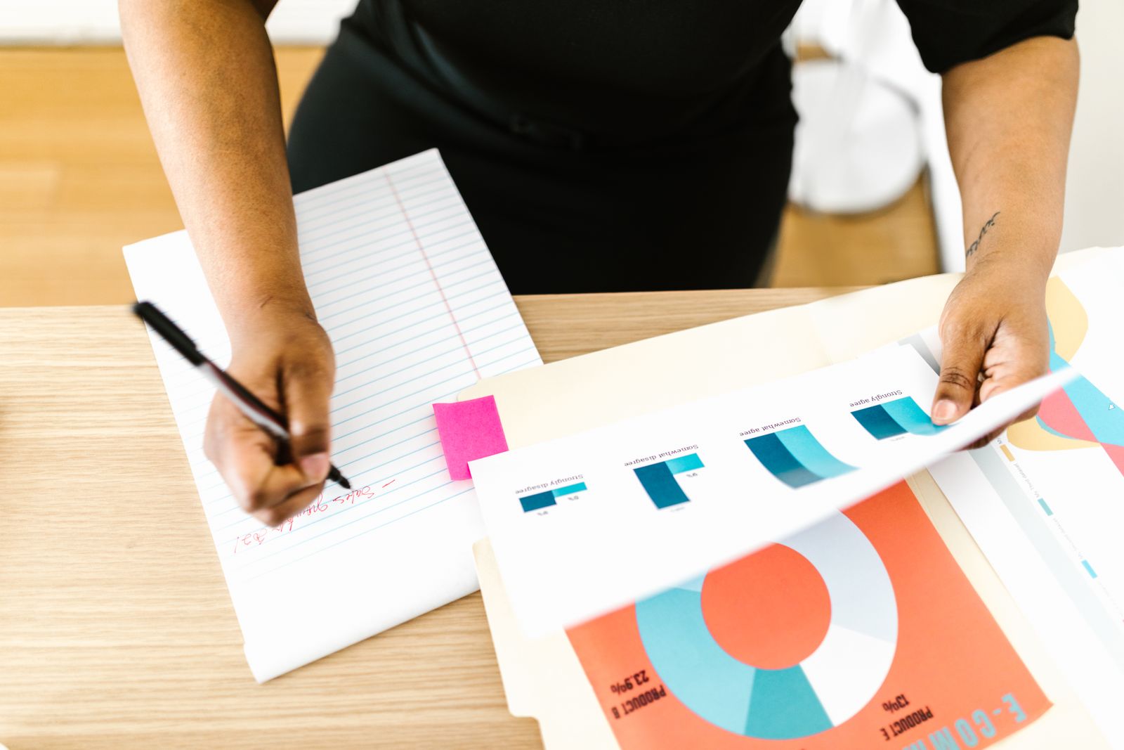 Person taking notes on a legal pad while reviewing printed bar and donut charts