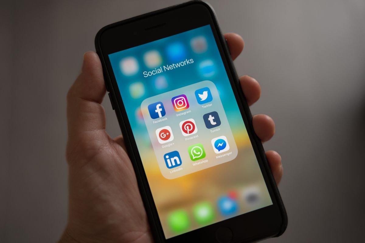 Author holding a smartphone showing social media apps used to build a book audience