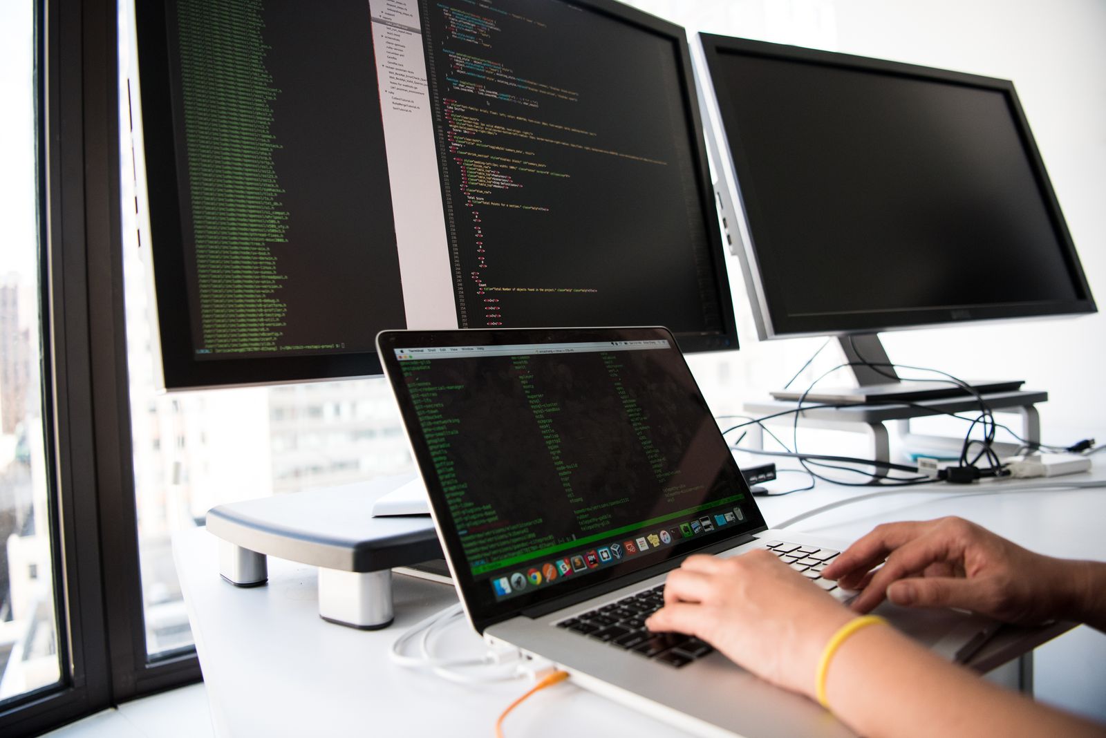 A developer working across a laptop and external monitors filled with code