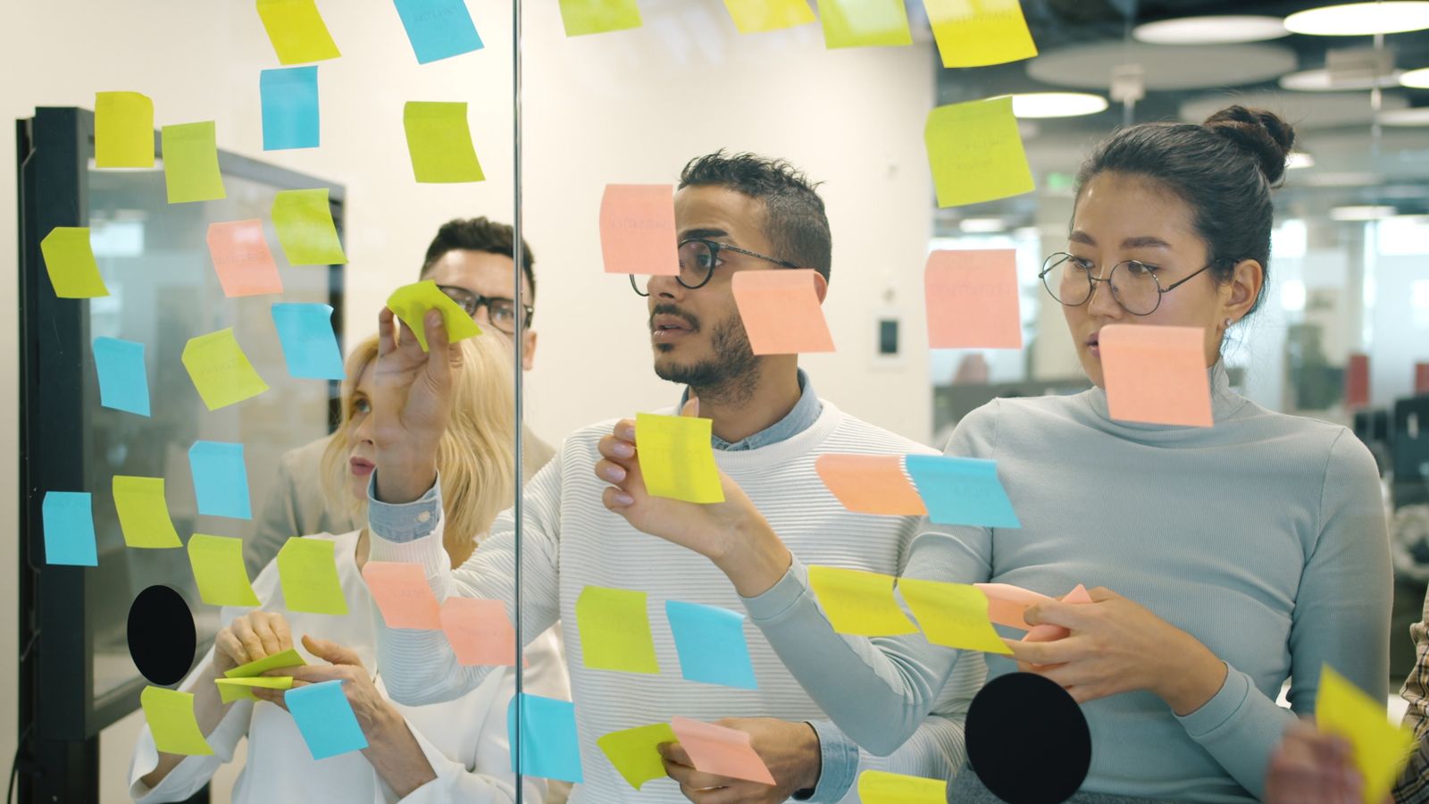 Team arranging colored sticky notes on a glass wall during a planning session