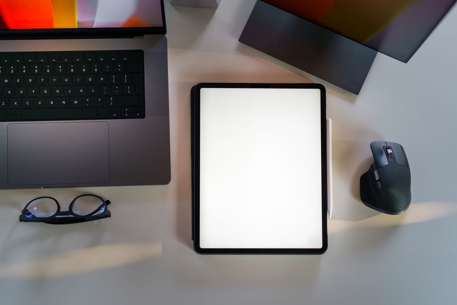 A laptop, a blank tablet, glasses, and a mouse on a white desk, ready for a website planning session