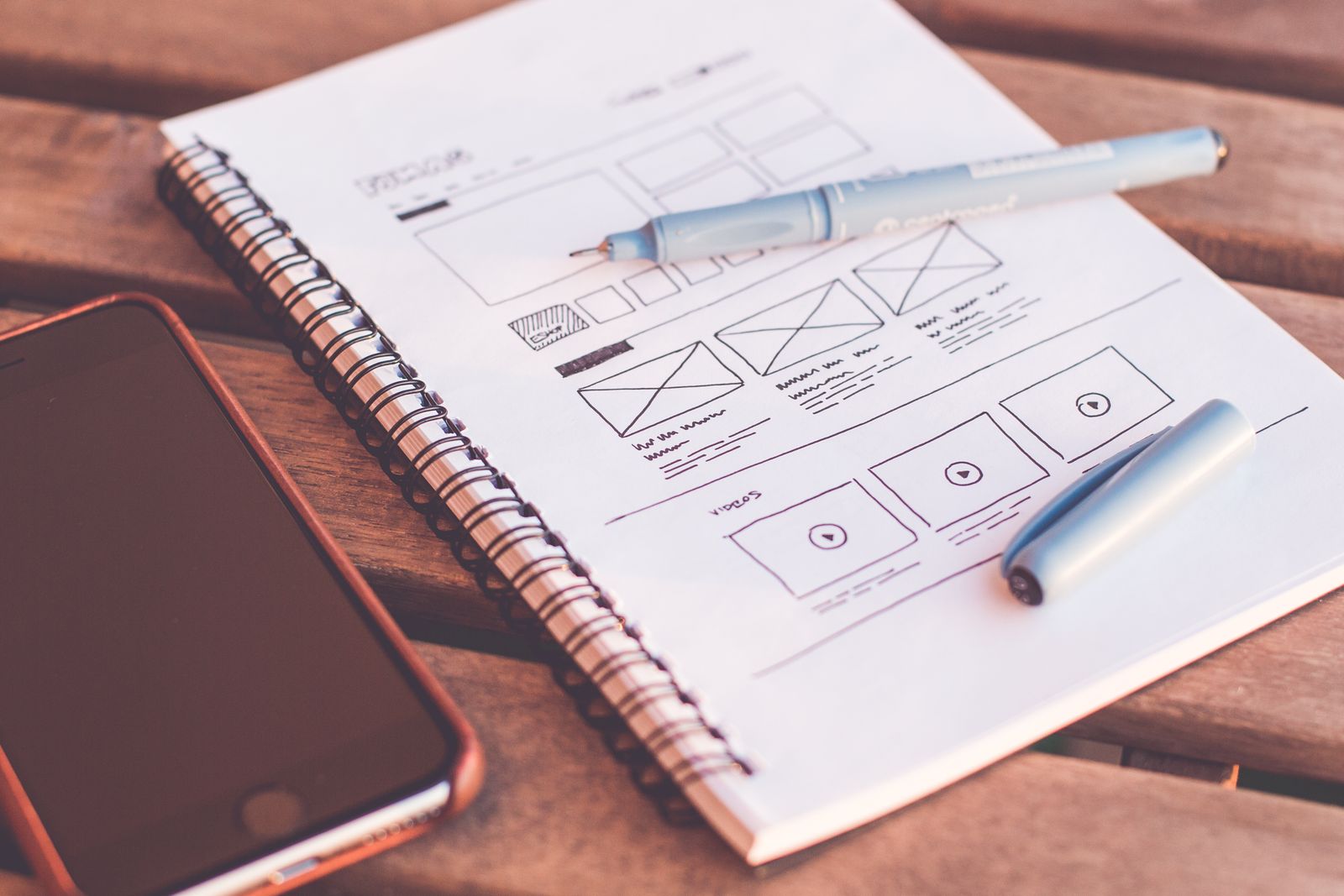 A hand-drawn website wireframe in a notebook next to a phone, the planning stage before choosing a platform