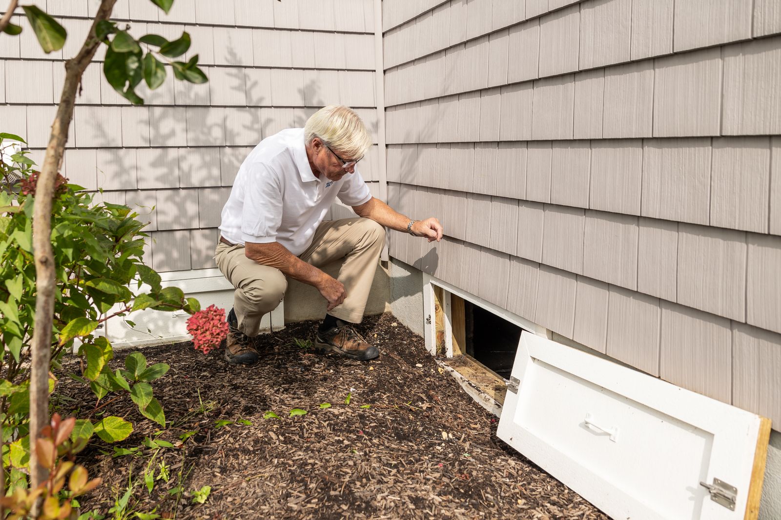 Pest control technician inspecting the crawl space vent of a home
